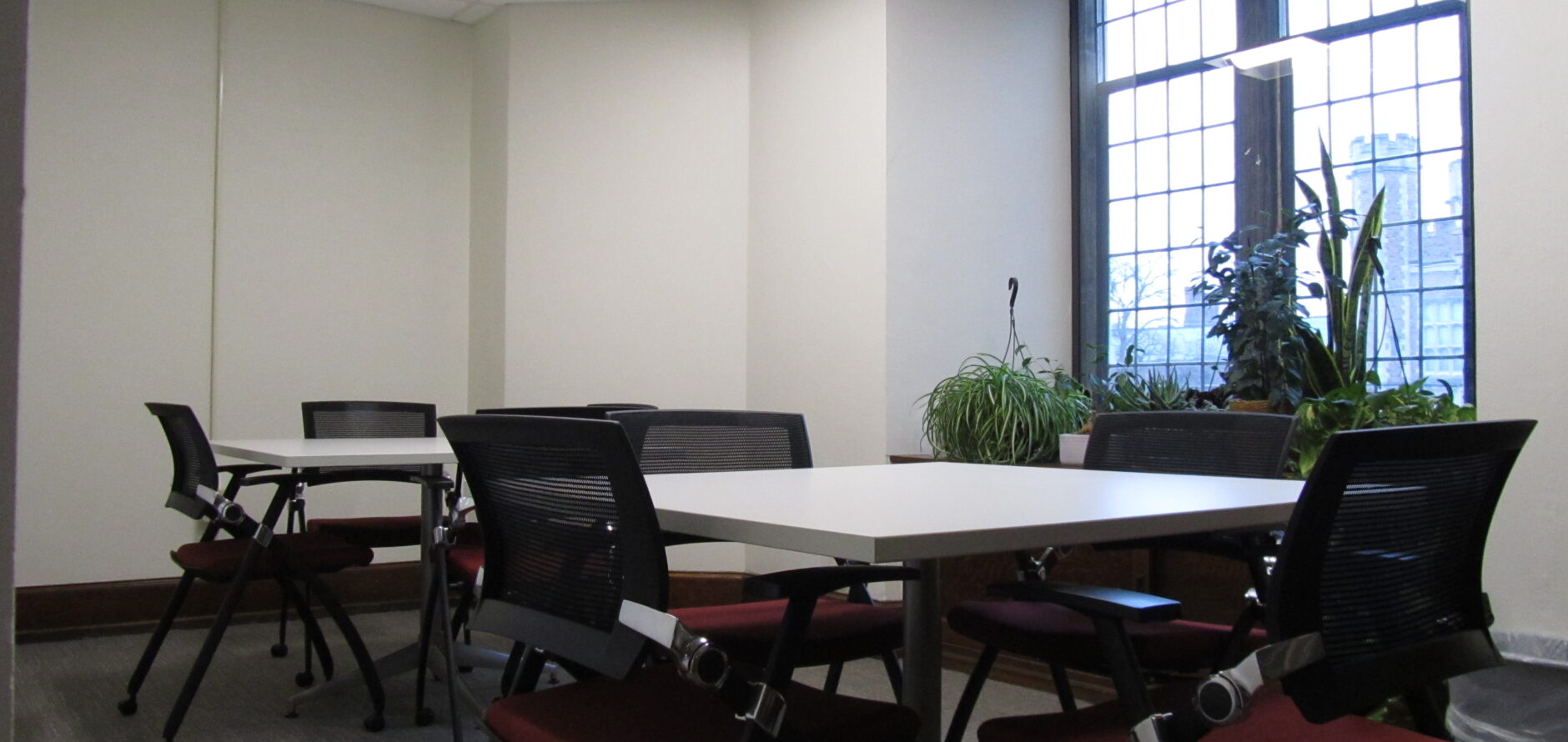 A study room with two tables and several chairs, there is a large window on one wall.