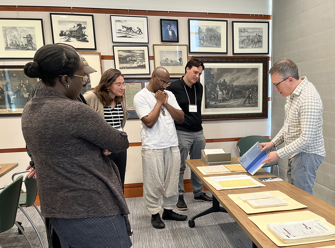 A group of five people stand around a sixth as they showcase physical poetry materials from Special Collections.