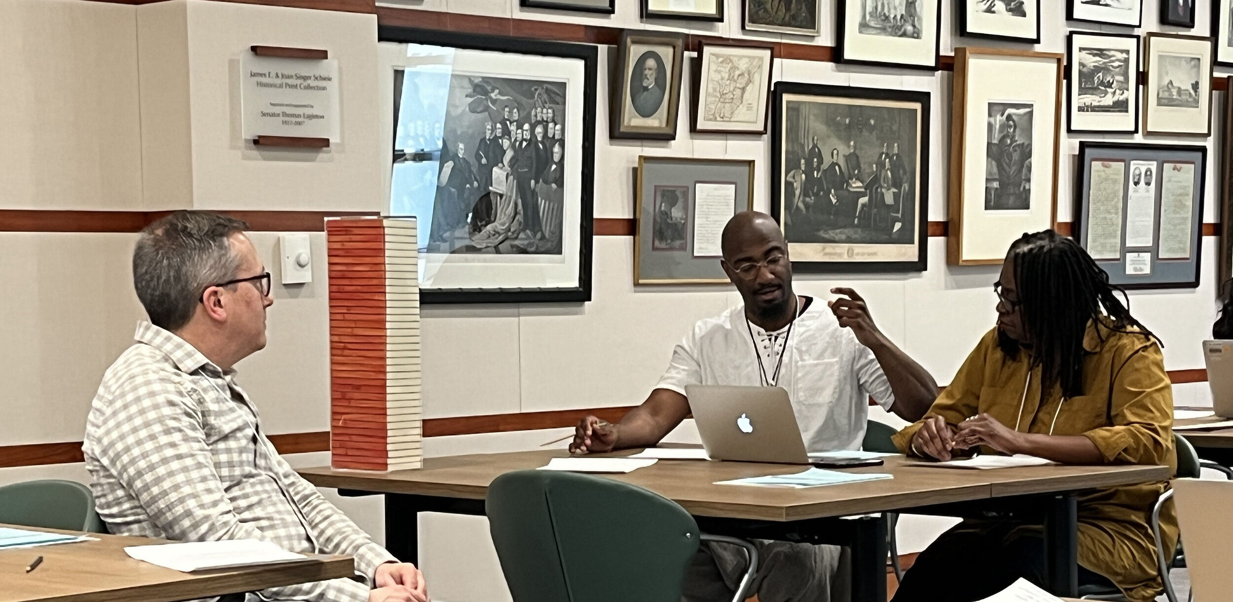 Two men and a woman sit at a table in conversation.