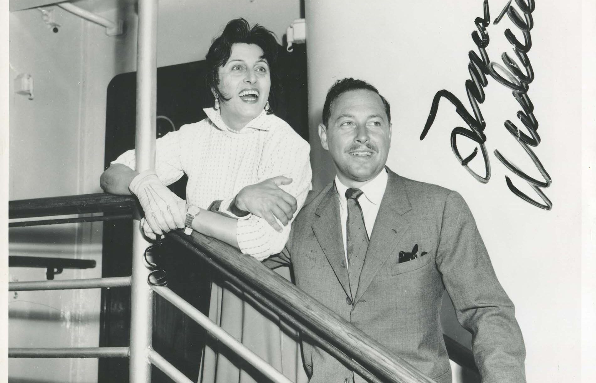 Anna Magnani and Tennessee Williams in the stairs of a ship facing the camera but looking away from the lens with elbows locked and excited expressions.