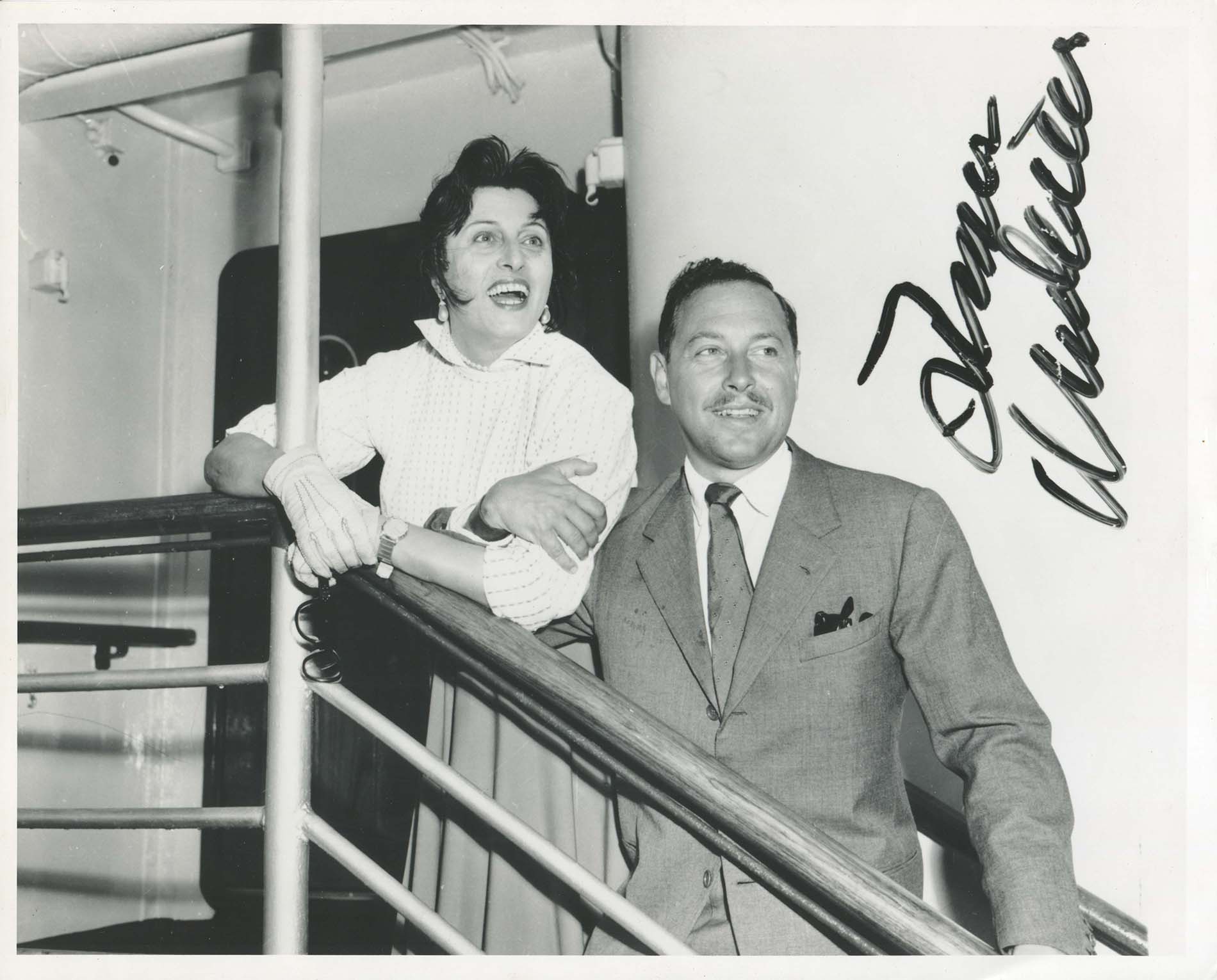 Anna Magnani and Tennessee Williams in the stairs of a ship facing the camera but looking away from the lens with elbows locked and excited expressions.