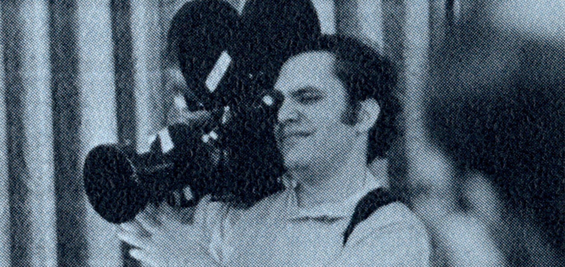 A man standing with a film camera on his shoulder and his eye on the view-piece.