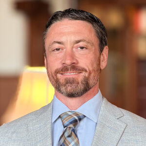 Staff photo of Christopher Galanos. Man in suit and tie looking at the camera.