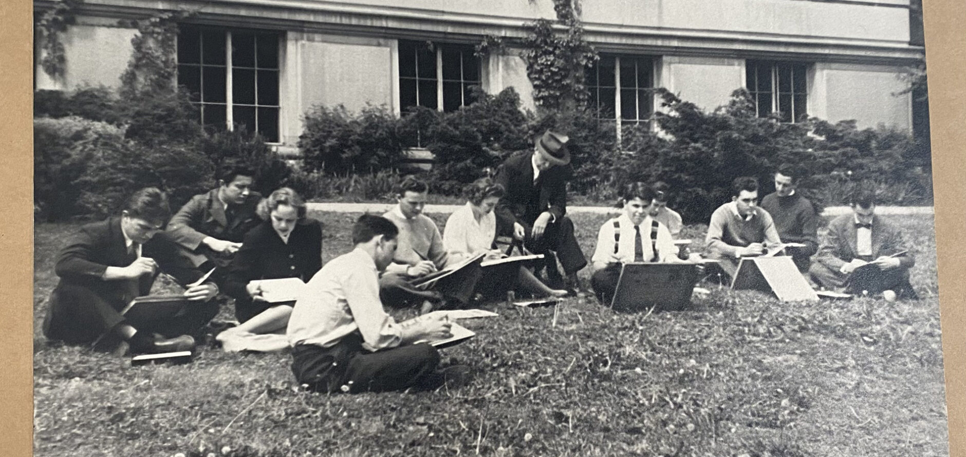 Eleven architecture students—nine men and two women—sketching outside on the lawn of Givens Hall while a professor sits nearby and instructs the class.