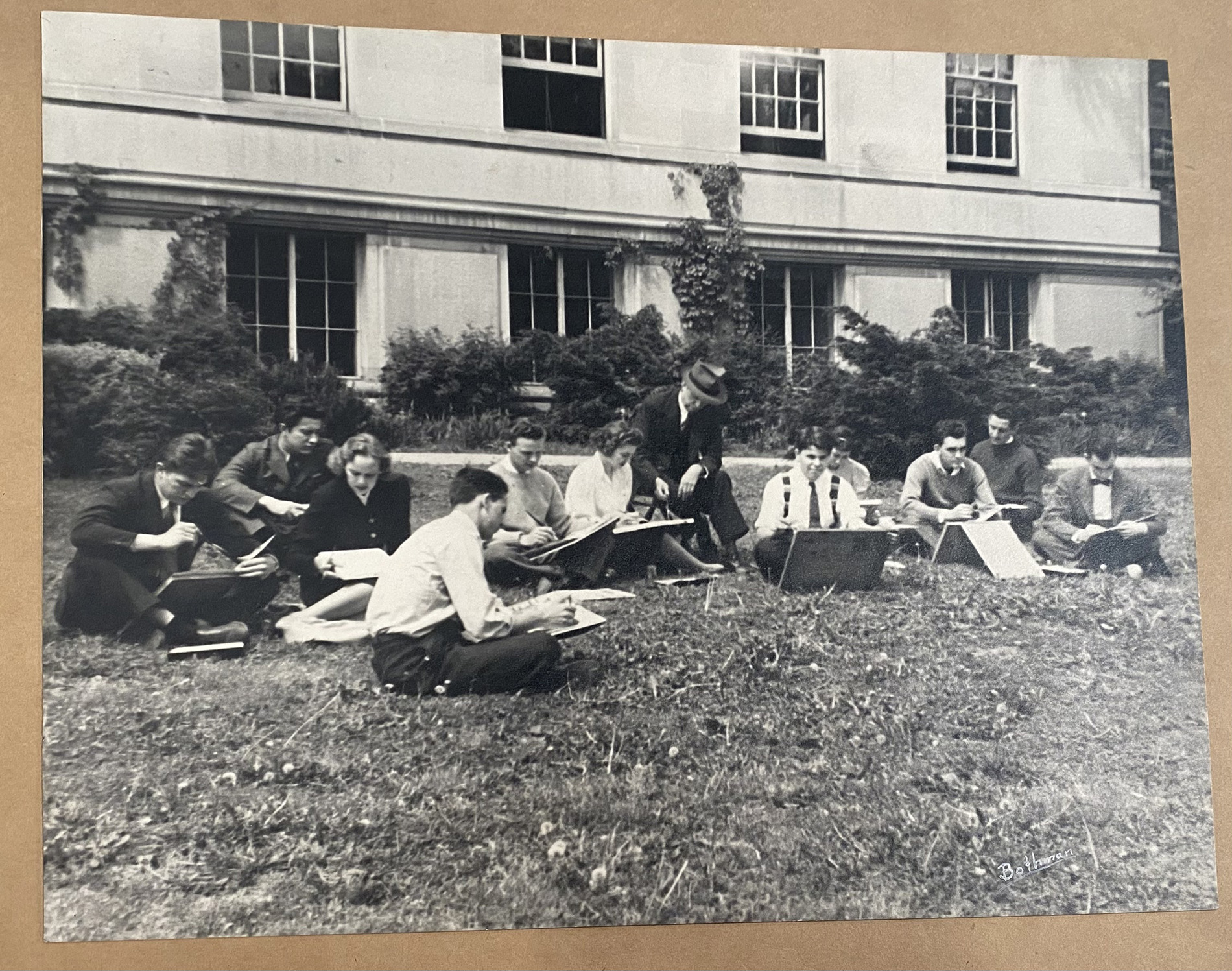 Eleven architecture students—nine men and two women—sketching outside on the lawn of Givens Hall while a professor sits nearby and instructs the class.