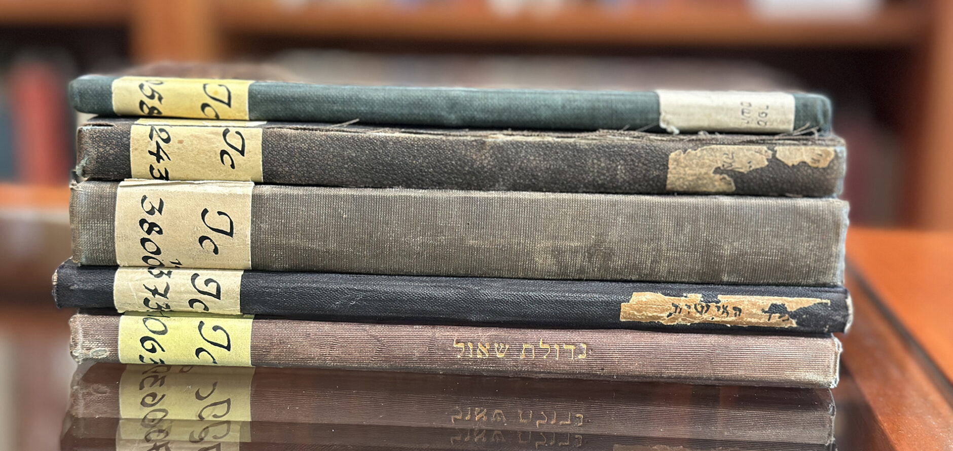 A collection of five Hebrew language books stacked on a glass tabletop.