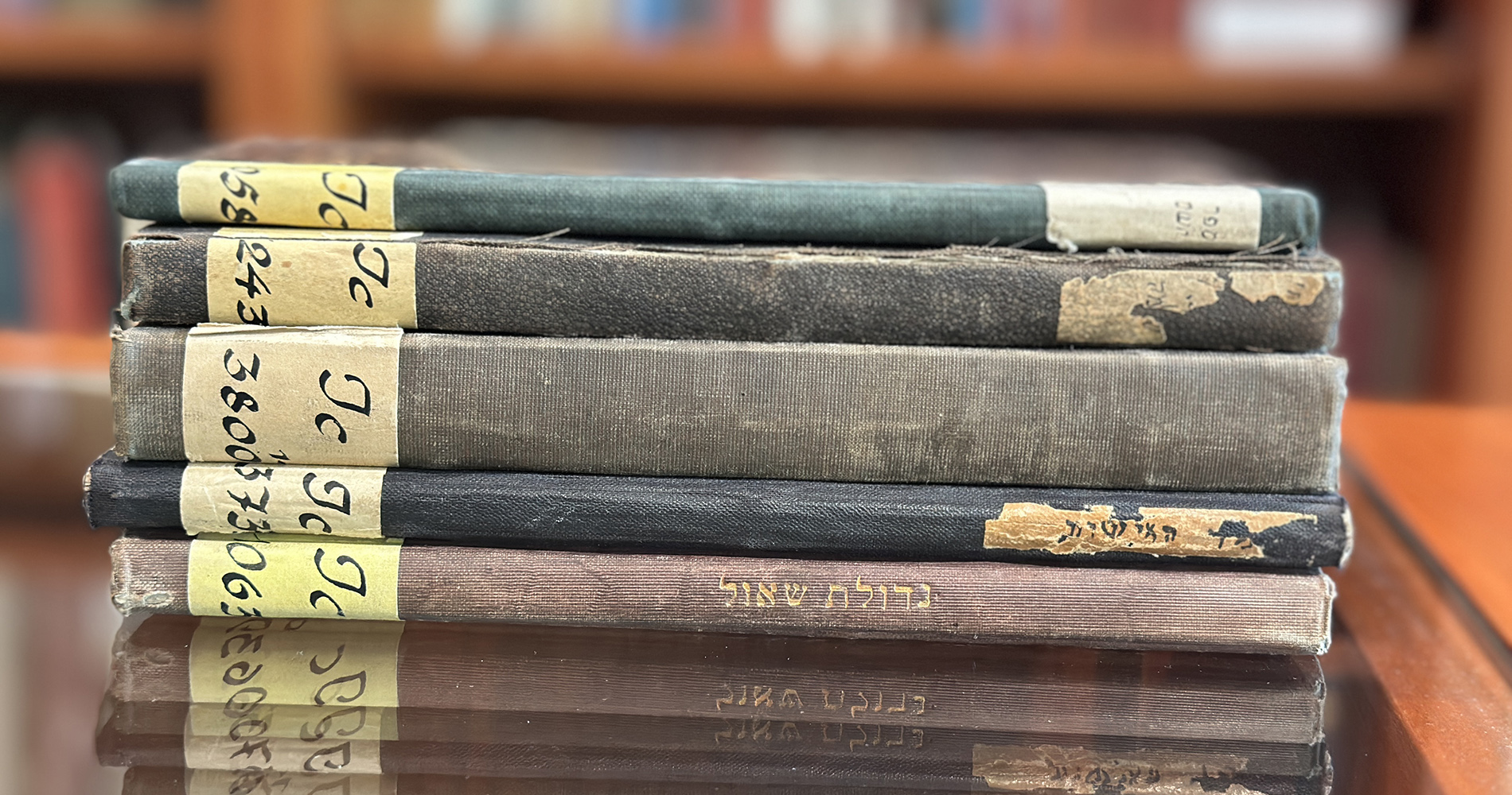 A collection of five Hebrew language books stacked on a glass tabletop.